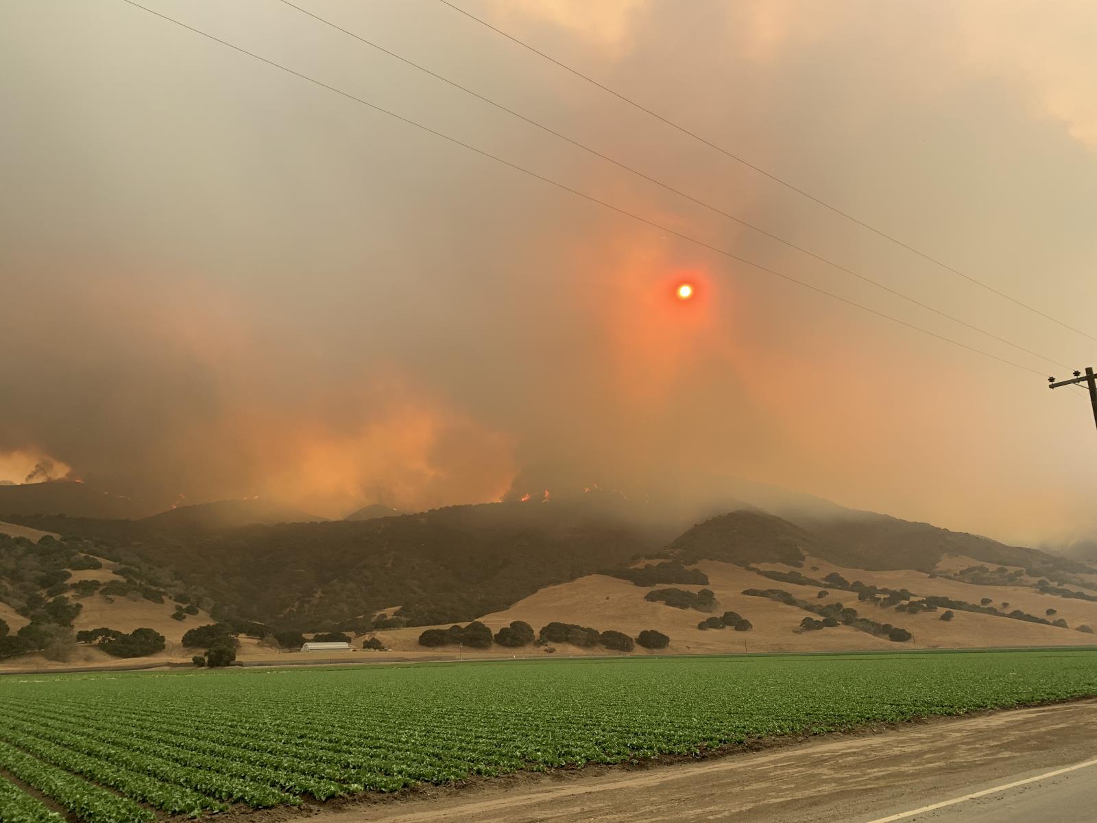 mountains with a smoke from a fire and at the foreground fields